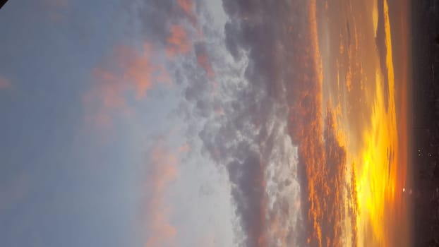 With the setting sun, the sky bursts into vibrant tones of amber and scarlet, adorned with expansive clouds, forming a mesmerizing scene with an intense fiery hue.