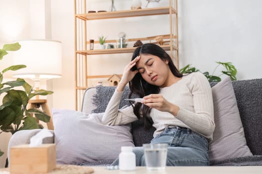 A woman feels unwell as she checks her temperature in a cozy living room illustrating the emotional experience of sickness.