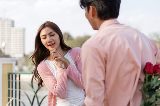 A couple shares a sweet moment as one surprises the other with roses on a sunny rooftop.