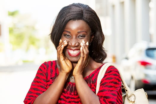 mature african woman standing outdoors looking at camera smiling with handbag.