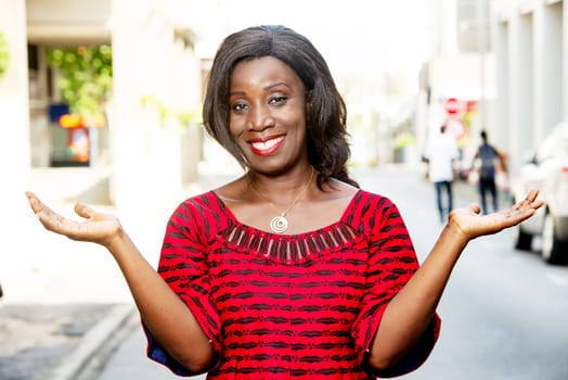 mature african woman standing outdoors looking at smiling with hands spread.