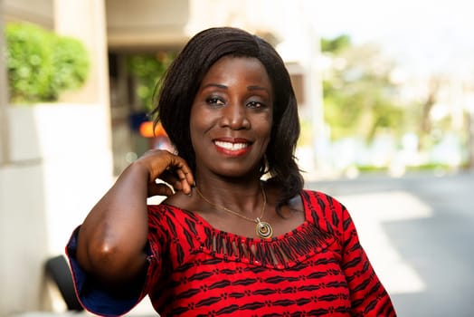 mature african woman standing outdoors looking at camera smiling.