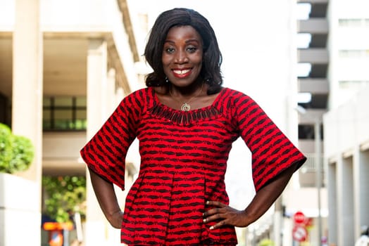 mature african woman standing outdoors looking at camera smiling.