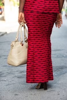 mature african woman standing outdoors giving back to camera with handbag.