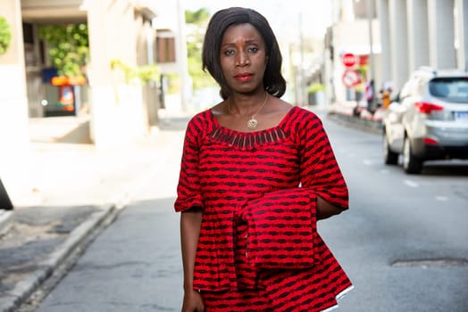 portrait of fashionable african woman posing in red loincloth standing on street in sunny daylight.