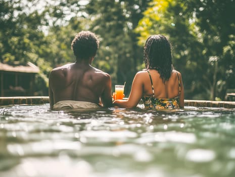 Back view of a couple sitting in a pool, holding drinks, and enjoying a relaxing moment surrounded by lush tropical greenery.