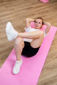 Woman doing floor exercises on a pink mat in a bright, plant-filled room