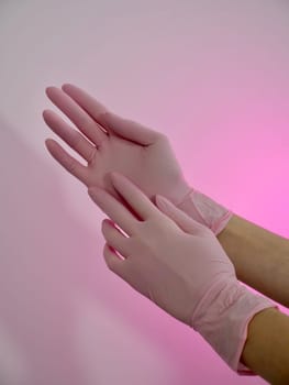 Female cosmetologist nurse wearing pink close-up medical gloves on white background, vertical, slow motion