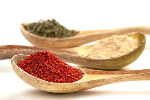 A close up of wooden spoons filled with red pepper powder, garlic powder, and basil leaves.