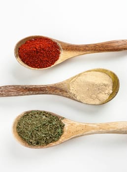 An overview of wooden spoons filled with red pepper powder, garlic powder, and basil leaves.