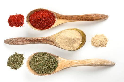 An overview of wooden spoons filled with red pepper powder, garlic powder, and basil leaves.