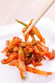 A close up image of sliced cucumbers mixed in red pepper paste and chopsticks.