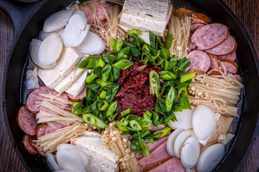A close up of a modern Korean dish using sausage, tofu, onions, mushrooms, and red pepper paste.