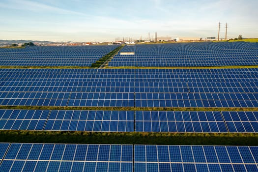 Drone view of blue solar panels on agricultural field during sunny day. The landscape is fully equipped with green renewable energy generators.