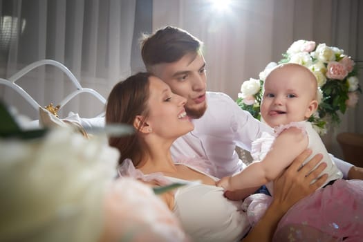 A couple enjoys a tender moment while their baby girl plays with a toy in a warm, inviting space filled with soft lighting on bed in beautiful room