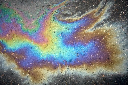 Vibrant gasoline spill producing a rainbow sheen on the asphalt parking lot.