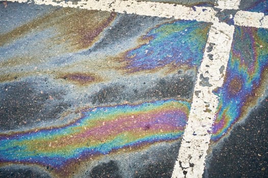 Gasoline or oil spill creating rainbow sheen on asphalt parking lot surface.