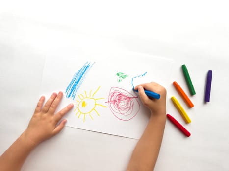 Childs hand drawing with colorful crayons on white paper. Creativity and imagination in action.