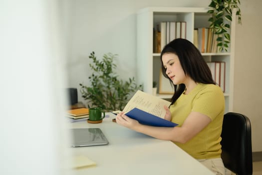 Beautiful young woman reading a book with focus in cozy home.