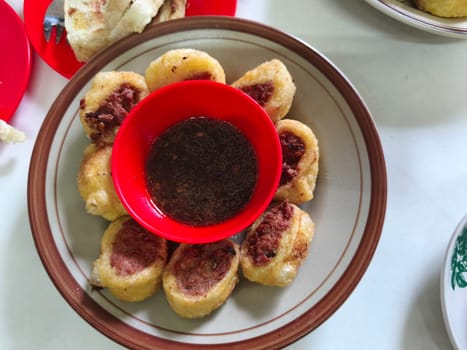 A plate of crispy golden brown gohiong filled with a meaty mixture, served with a small bowl of dipping sauce.