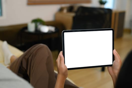 Closeup of hands holding digital tablet with a blank display lying on sofa.