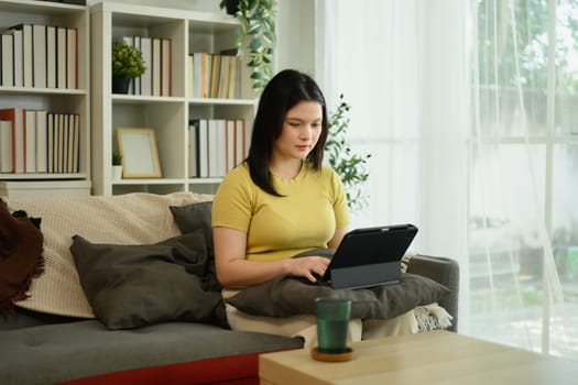 Focused young female freelancer working with her digital tablet at home.