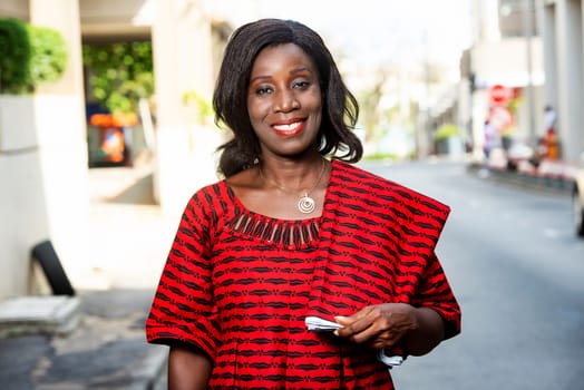Stylish African woman in fashion, wearing a red loincloth and standing on a street in a sunny day.
