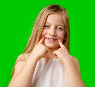 Young girl smiling playfully and making funny faces against a bright green background in studio