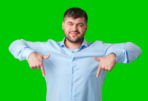 Man in a blue striped shirt and jeans gesturing downward against a bright green background in studio