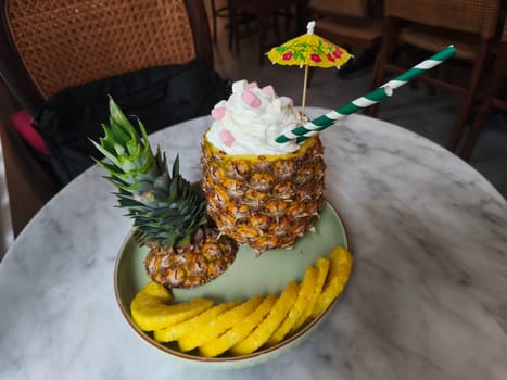 A refreshing pineapple cocktail served in a hollowed out pineapple, topped with whipped cream and a colorful umbrella. A Pinacolada