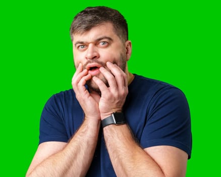 A surprised man with a beard and blue shirt making an astonished face against a vibrant green background in studio