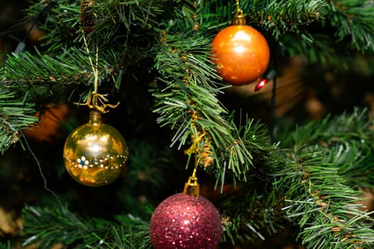 Colorful ornaments in gold, orange, and purple decorate a lush green Christmas tree, bringing warmth and cheer to the holiday atmosphere. The vibrant colors enhance the festive spirit.