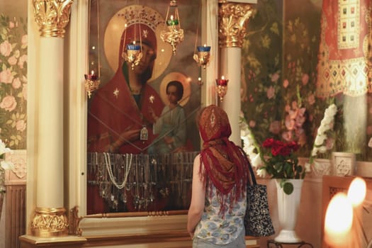 Russian woman in red headscarf praying in front of icon