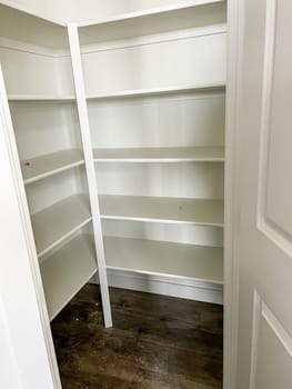 A clean and empty pantry space with built-in white shelves in a newly constructed home The room features fresh white paint and dark wooden flooring highlighting its modern and functional design