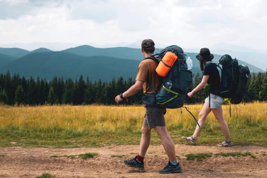 A young happy couple in love, a guy and a girl with a tourist backpack and equipment go on a trip, walk along trails, forest and mountains , friends actively spend time together in nature outdoor.