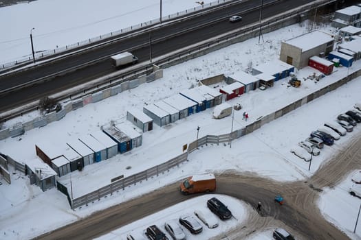 A snowy construction site featuring multiple containers, various vehicles, and a busy adjacent highway nearby