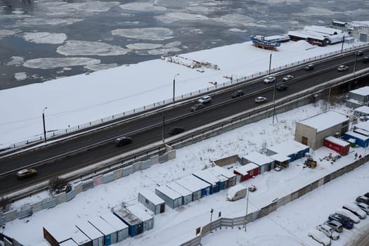 An aerial view shows a snowy road by a river with ice, highlighting the enchanting beauty of winter