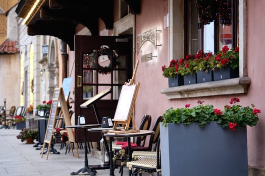 Colorful potted flowers decorate the outdoor area of a caf nestled in a quaint street. Tables and chairs await guests as soft evening light enhances the inviting atmosphere.