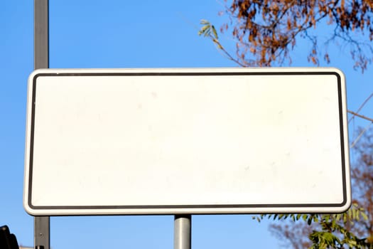 A blank street sign stands alone, surrounded by a peaceful neighborhood. The bright blue sky serves as a backdrop, creating a serene atmosphere.