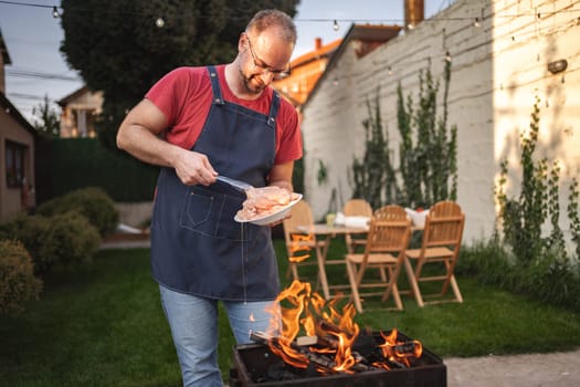A person barbecuing chicken outdoors in a vibrant garden setting.
