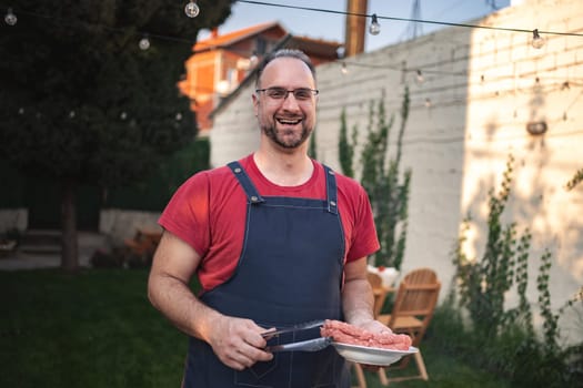 A smiling cook holds ground meat while enjoying the outdoor cooking experience.