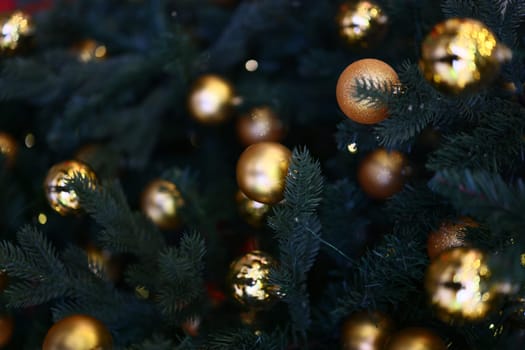 A closeup view of shimmering golden ornaments beautifully adorning a richly green Christmas tree, sparkling