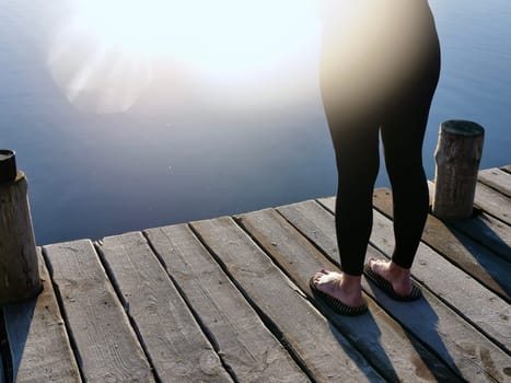 Woman standing on sadhu board, process of standing barefoot on nails, view of feet practicing yoga and meditation outdoors, autumn day near lake at sunrise