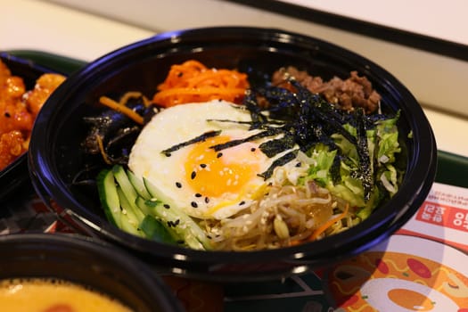 A vibrant and colorful bowl of bibimbap featuring a perfectly cooked sunnysideup egg, fresh vegetables, and seaweed