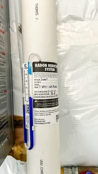 Parker, Colorado, USA-January 11, 2023- A close-up view of a radon reduction system installed in the basement of a newly constructed residential home. The system features a labeled pipe with installation details and a manometer to monitor air pressure, ensuring safe indoor air quality.