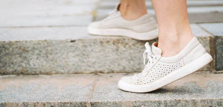 A girl walks in the city, steps of a staircase, close-up view of her feet with stylish white sneakers on, comfortable casual shoes.