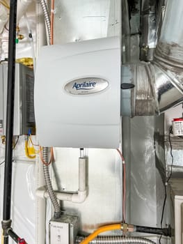 Castle Pines, Colorado USA - January 18, 2023-Aprilaire whole-home humidifier installed on HVAC ductwork in a new residential basement. The unit is connected to pipes and electrical systems, ensuring proper humidity control throughout the house.
