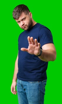 A man with a serious expression holds up both hands in a stopping gesture against a bright green background in studio