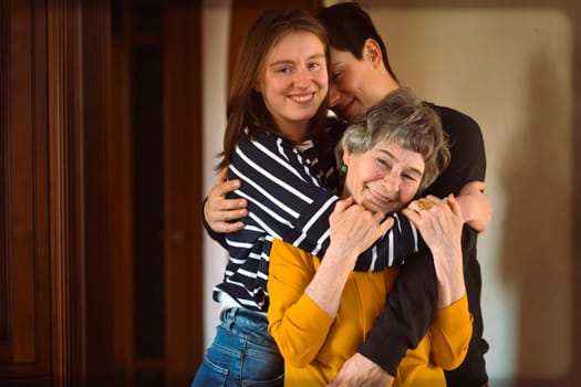 Young man and a girl happily hug their grandmother, the family lovingly takes care of their elderly parents and congratulates them on the holiday, the grandson with his sister visit an elderly woman.