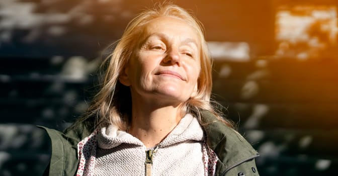 An elderly 60 beautiful woman with a kind smile is walking outdoors on a sunny autumn day, a happy old lady, a grandmother takes care of her appearance, natural beauty with wrinkles portrait closeup.